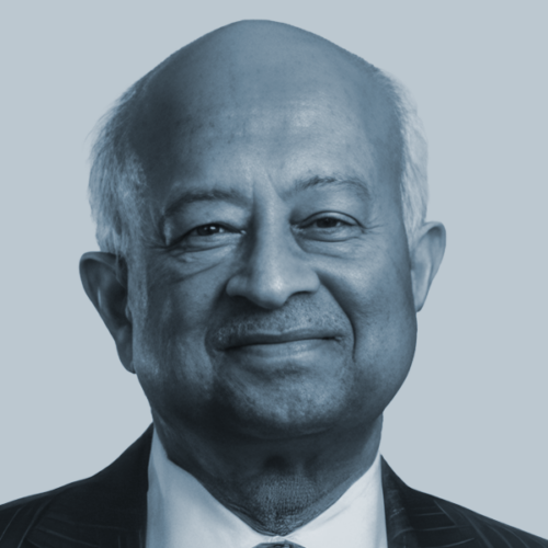 Head-and-shoulders portrait of a smiling older man in a suit, against a light blue background.